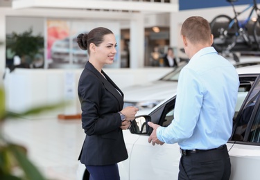 Photo of Young saleswoman working with client in car dealership