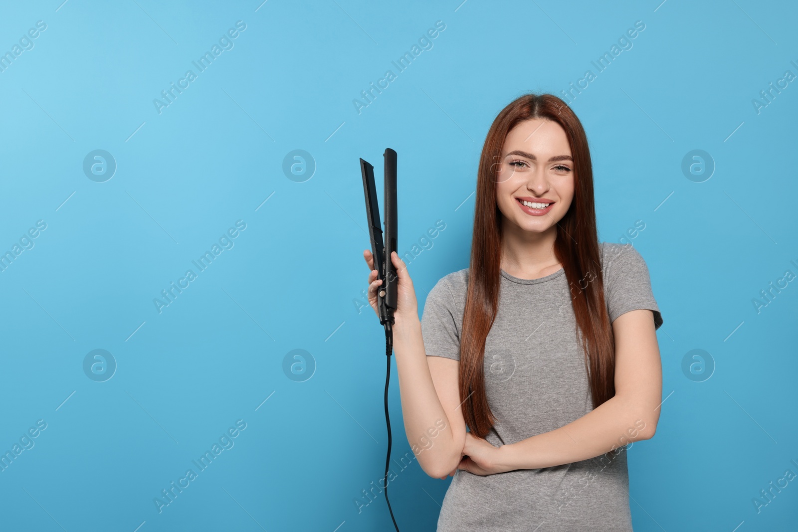 Photo of Beautiful woman with hair iron on light blue background, space for text