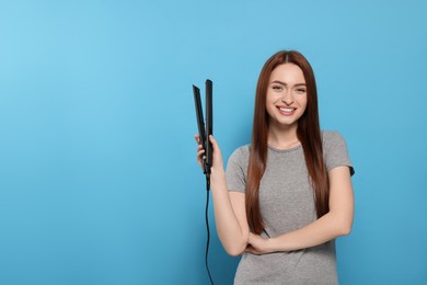 Photo of Beautiful woman with hair iron on light blue background, space for text