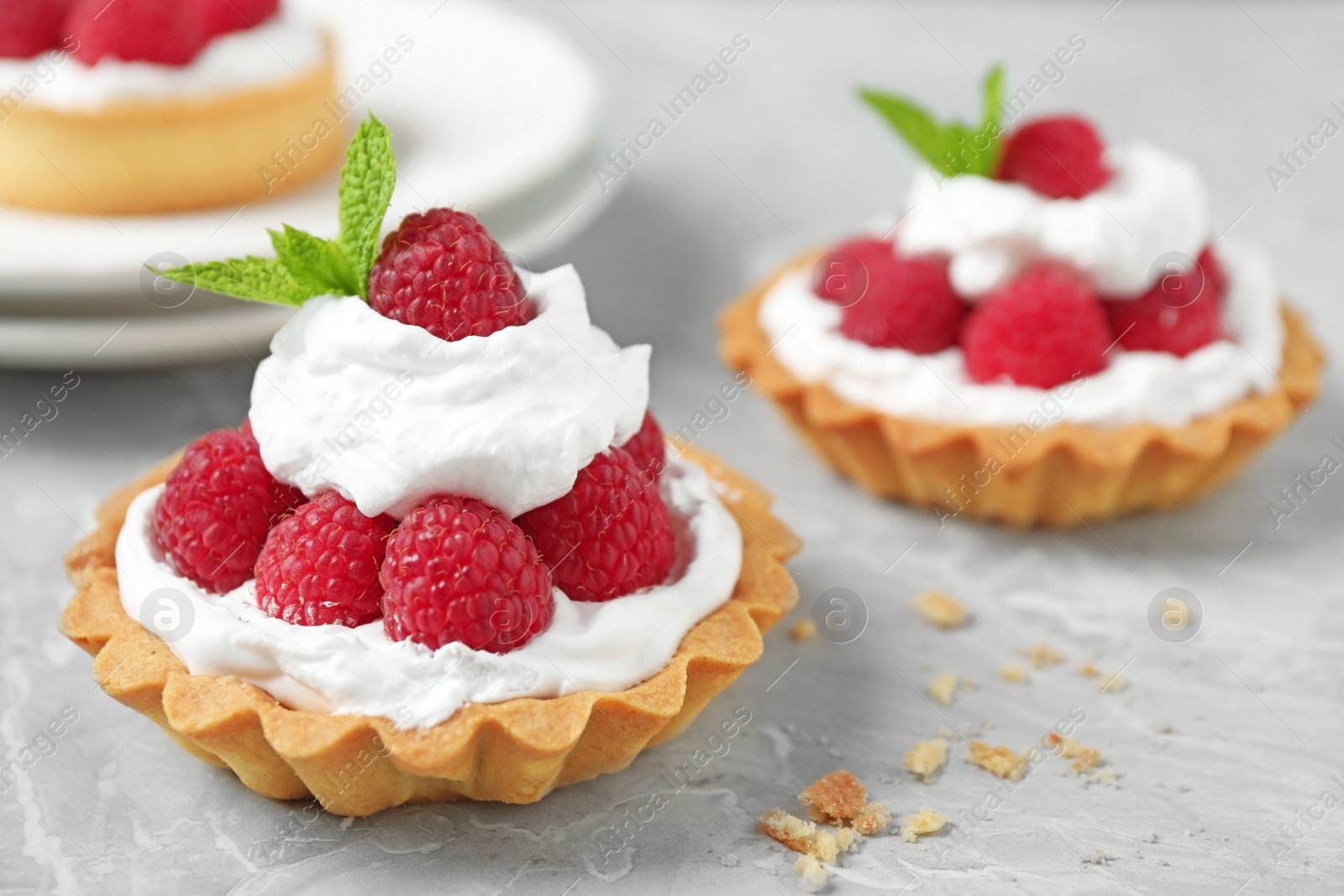 Photo of Tarts with raspberries on marble table, closeup. Delicious pastries