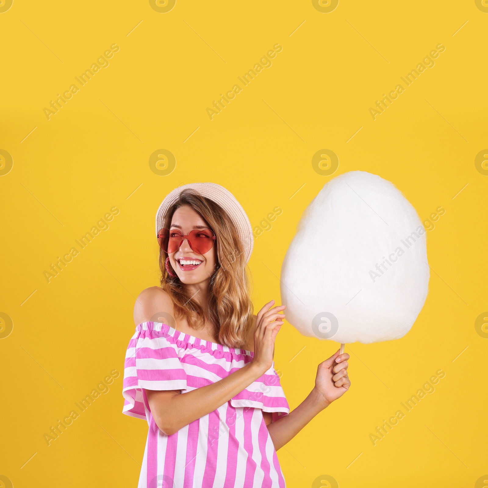 Photo of Happy young woman with cotton candy on yellow background