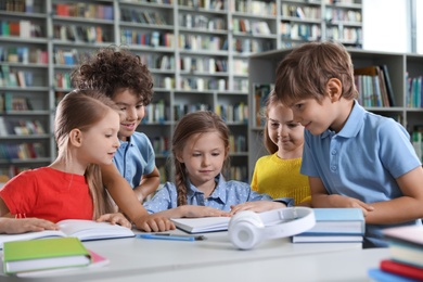 Photo of Group of happy little children reading books at table in library