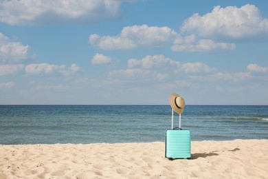 Photo of Turquoise suitcase with straw hat on sandy beach near sea, space for text