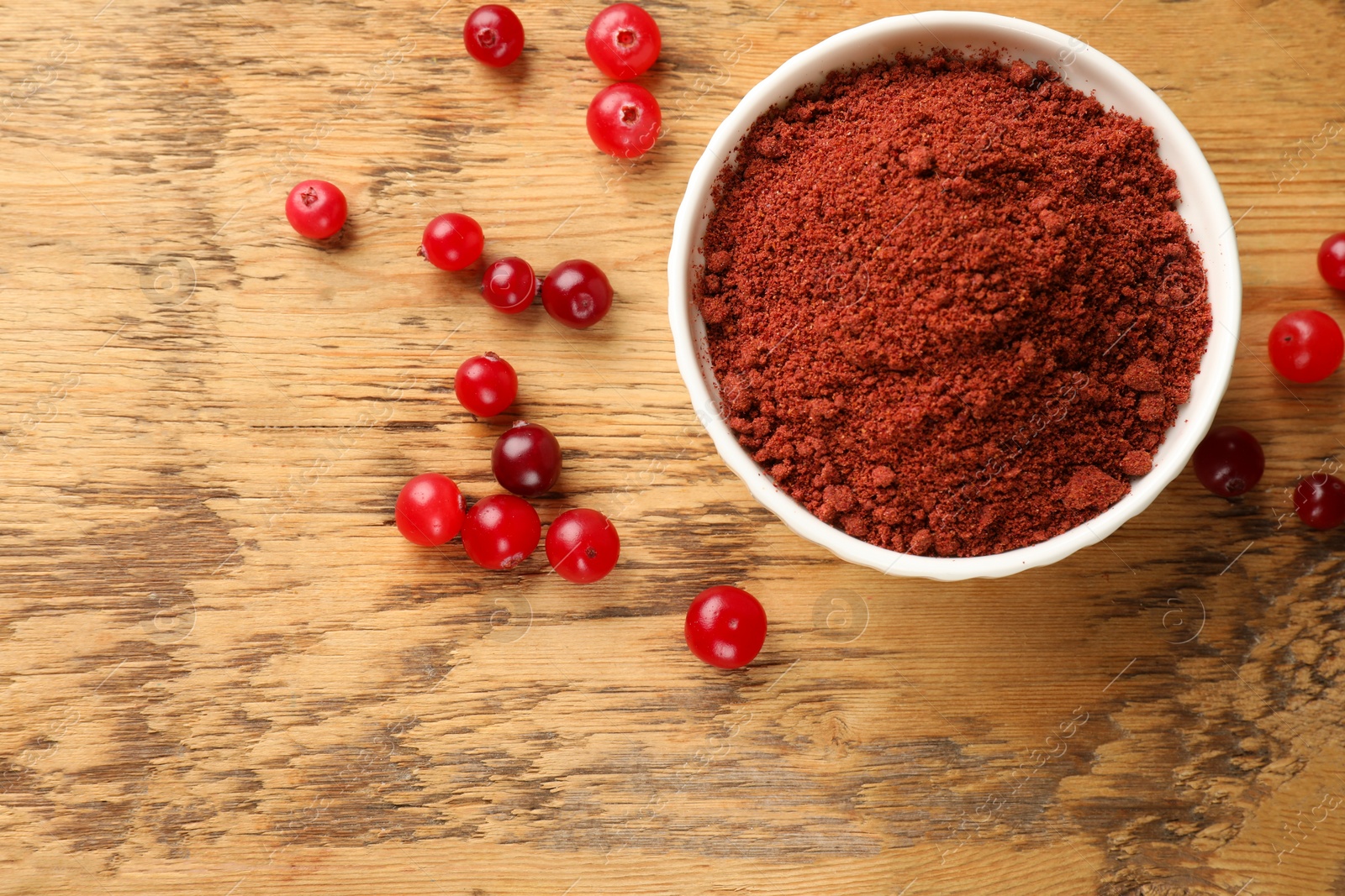 Photo of Dried cranberry powder in bowl and fresh berries on wooden table, top view. Space for text