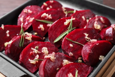 Photo of Raw beetroot slices, garlic and rosemary in baking dish, closeup