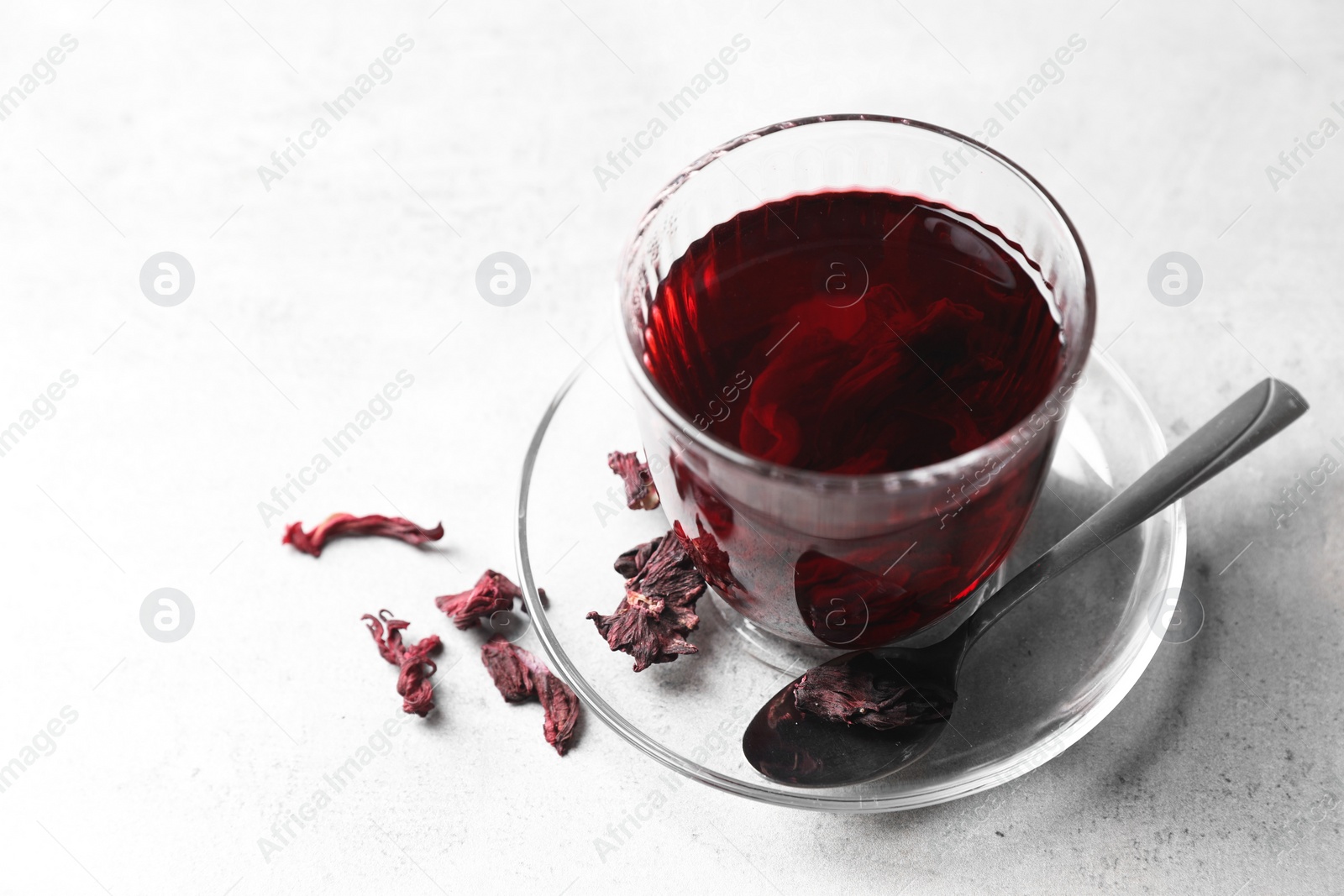 Photo of Aromatic hibiscus tea in glass, dried roselle calyces and spoon on light table, closeup and space for text
