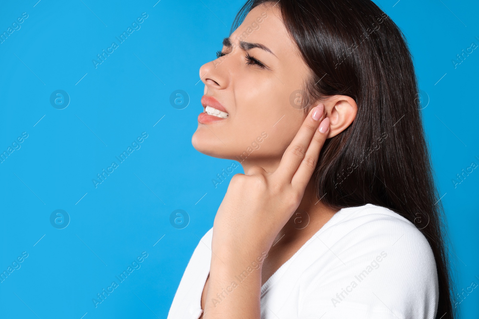 Photo of Young woman suffering from ear pain on light blue background, space for text