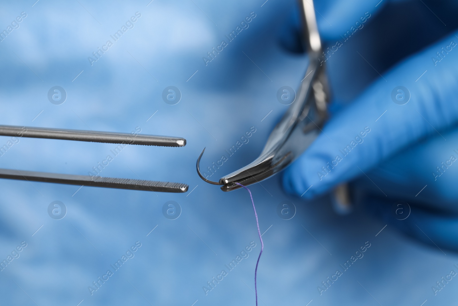 Photo of Professional surgeon holding forceps with suture thread, closeup. Medical equipment