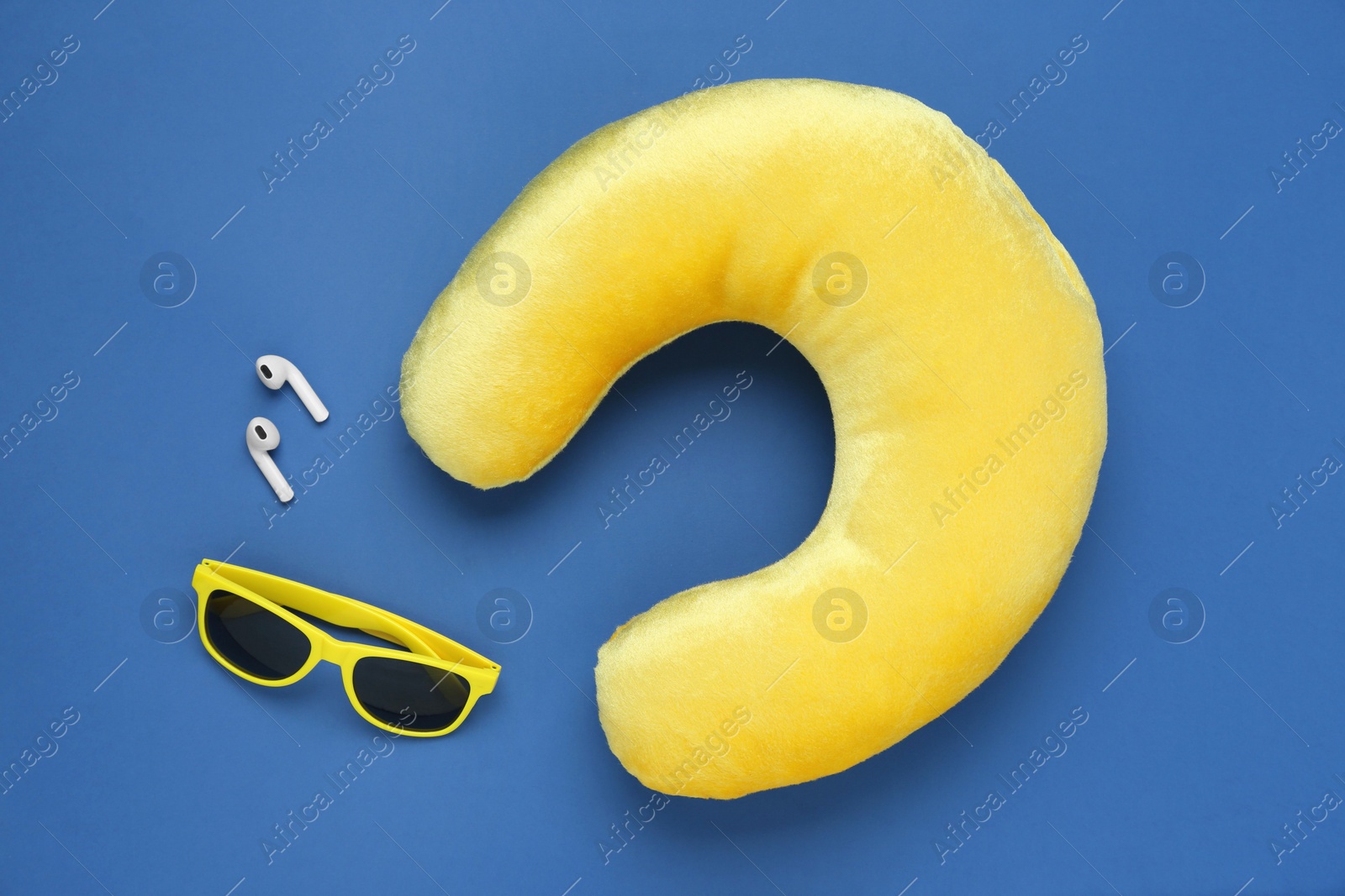 Photo of Yellow travel pillow, sunglasses and earphones on blue background, flat lay