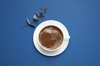 Photo of Classic black coffee and eucalyptus on blue background, top view. Color of the year 2020
