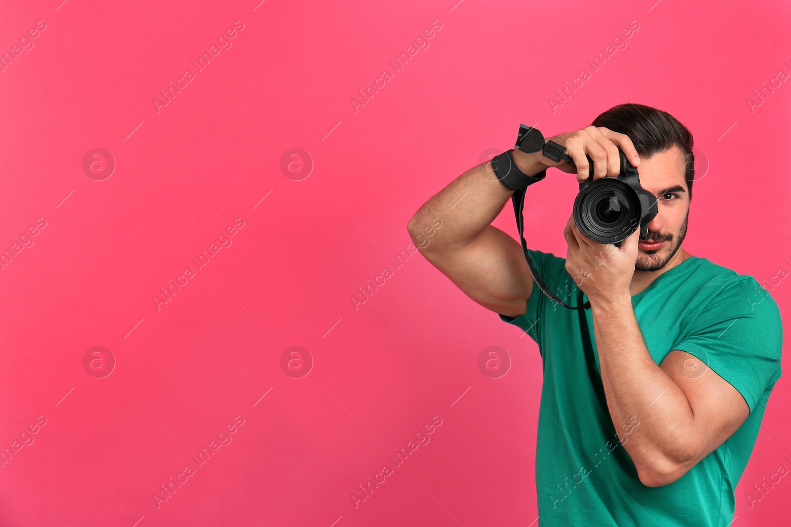 Photo of Young professional photographer taking picture on pink background. Space for text