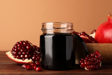 Photo of Glass jar of tasty pomegranate sauce and fresh ripe fruit on wooden table