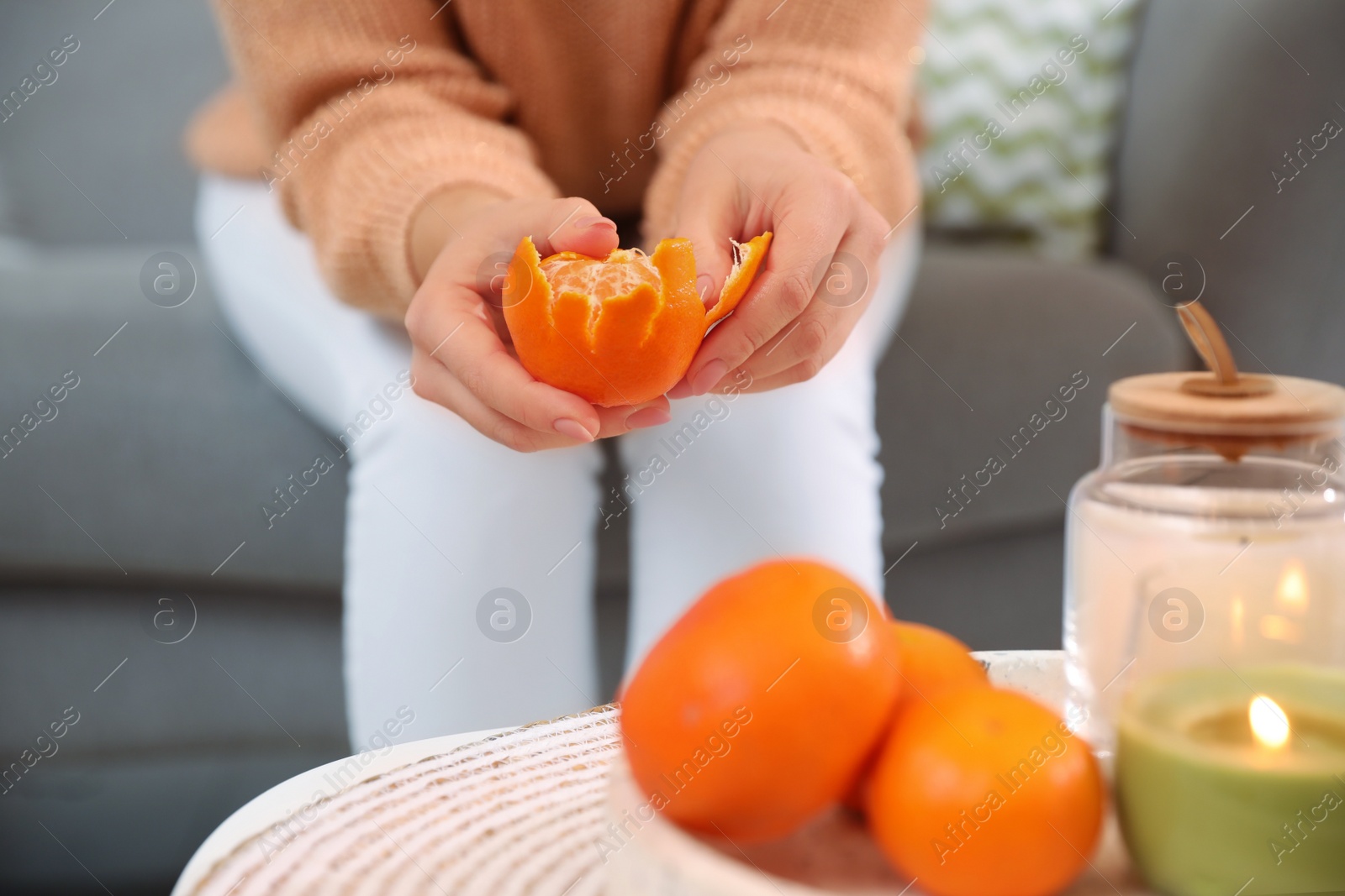 Photo of Young woman peeling fresh tangerine on sofa indoors, closeup