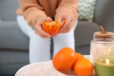 Young woman peeling fresh tangerine on sofa indoors, closeup