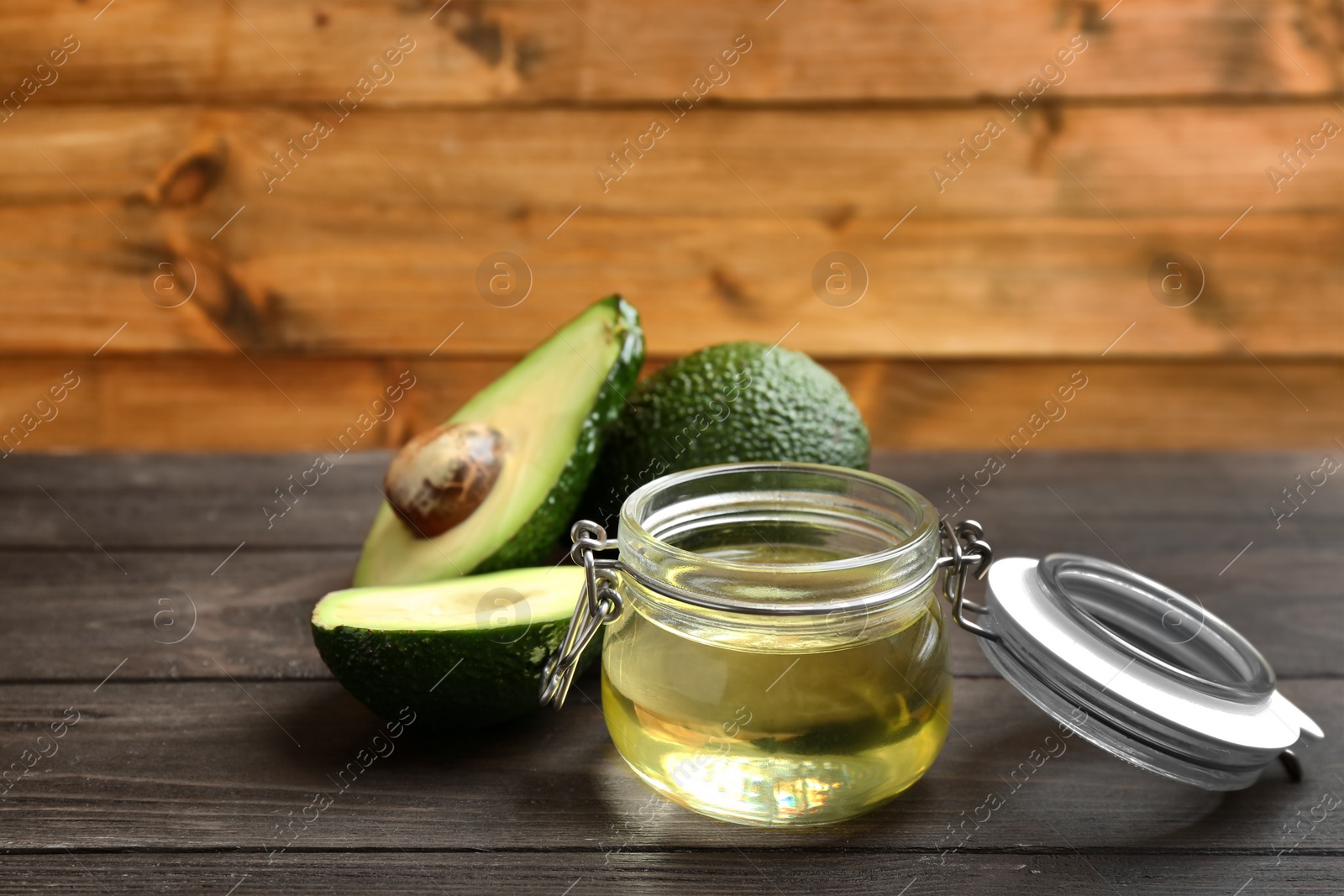 Photo of Jar of natural oil and avocados on wooden table. Space for text