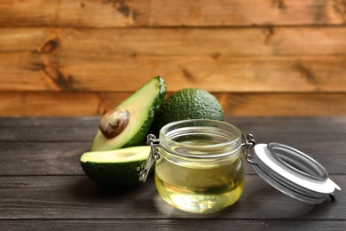 Jar of natural oil and avocados on wooden table. Space for text