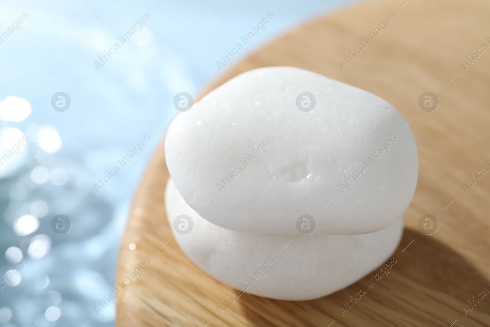 Photo of Spa stones on wooden surface against light blue background, closeup