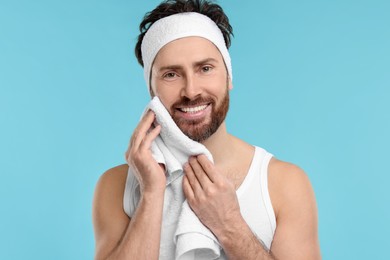 Photo of Washing face. Man with headband and towel on light blue background