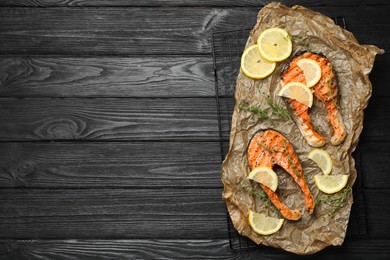 Photo of Tasty grilled salmon steaks and ingredients on black wooden table, top view. Space for text