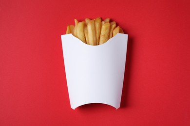 Photo of Paper cup with French fries on red table, top view