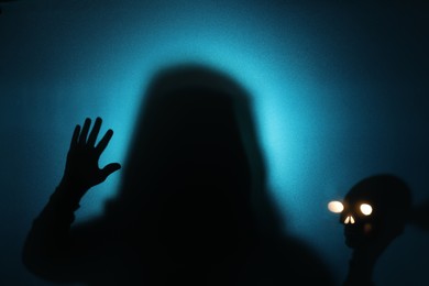 Silhouette of ghost and skull behind glass against blue background