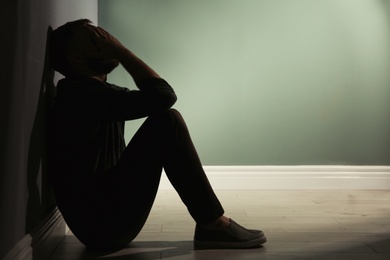 Photo of Depressed young man sitting on floor in darkness