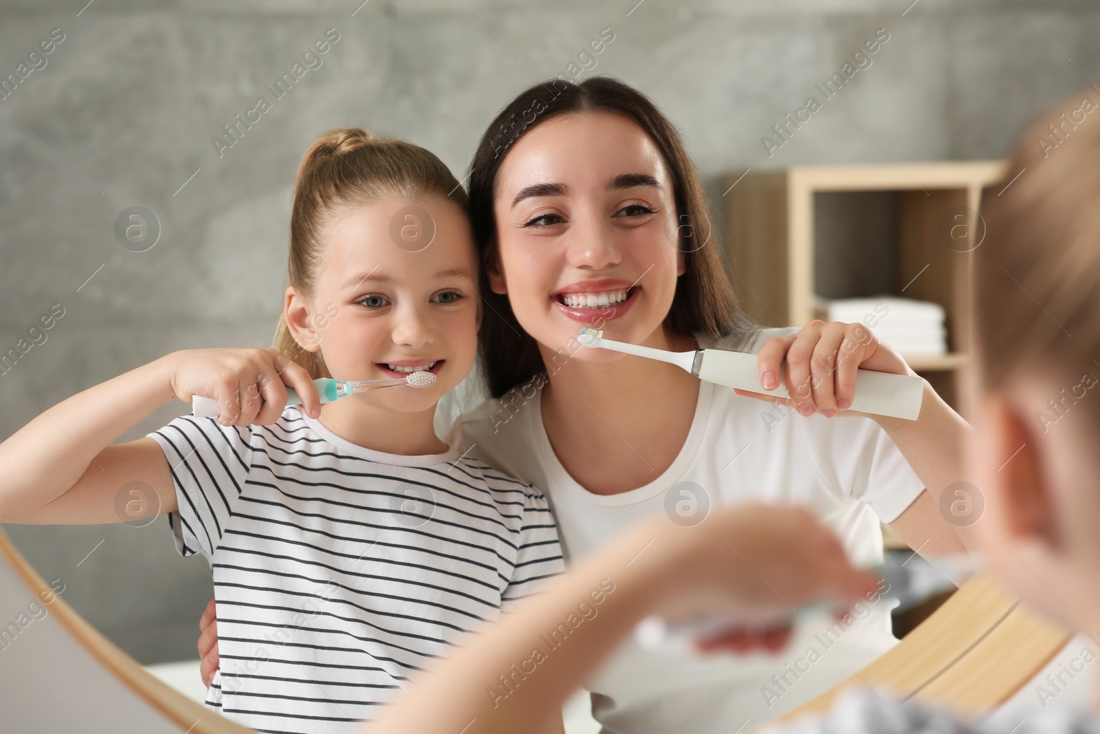 Photo of Mother and her daughter brushing teeth together near mirror in bathroom