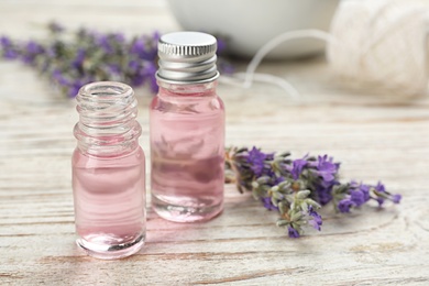 Photo of Bottles with natural lavender oil and flowers on white wooden table, closeup view. Space for text