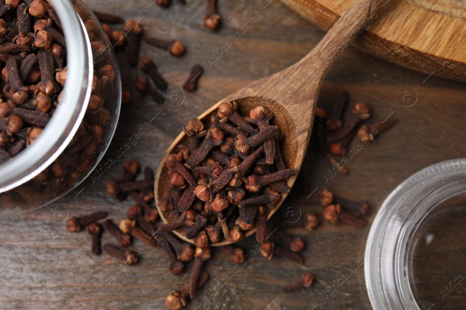 Photo of Glass jar and spoon with aromatic cloves on wooden table, flat lay