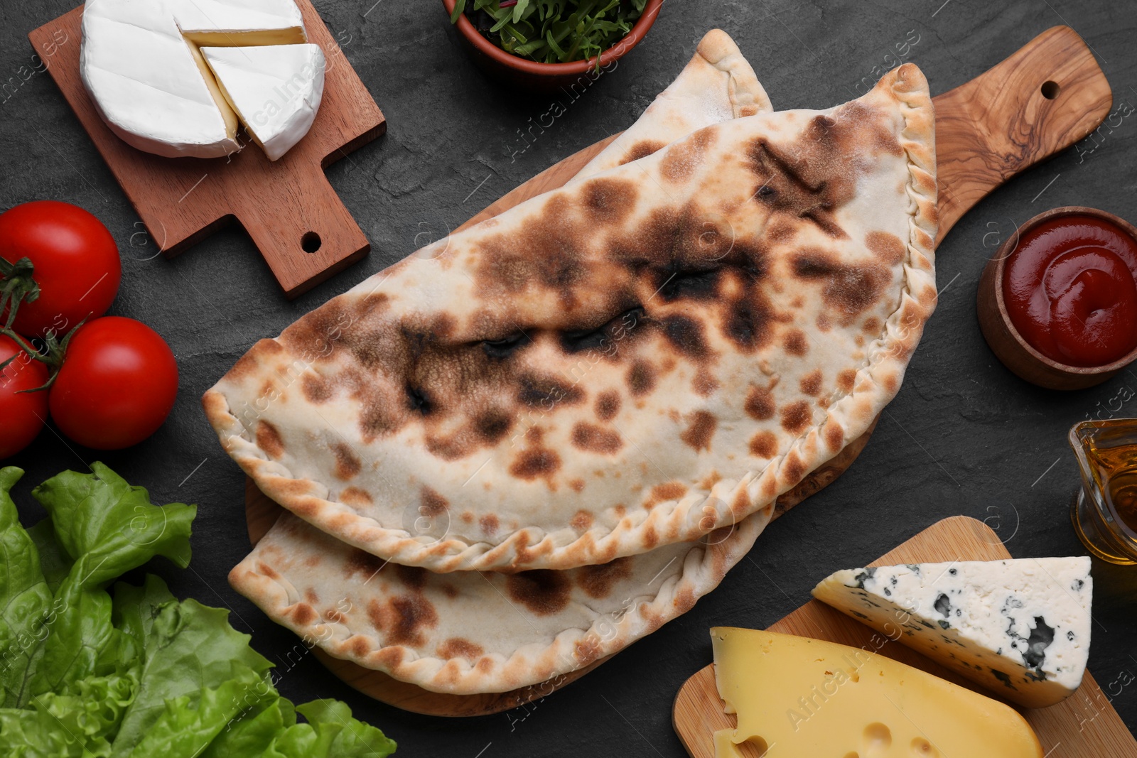 Photo of Delicious calzones and products on black table, flat lay
