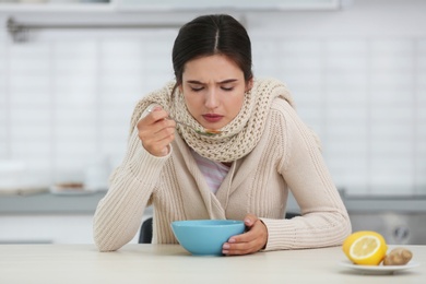 Sick young woman eating soup to cure flu at table in kitchen