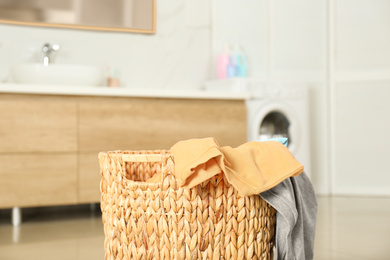 Photo of Wicker basket with dirty laundry in bathroom