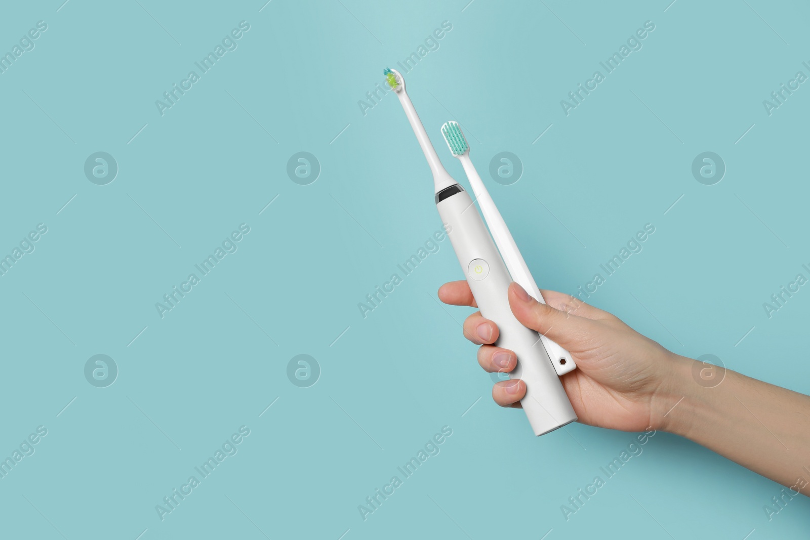 Photo of Woman holding electric and plastic toothbrushes on light blue background, closeup. Space for text