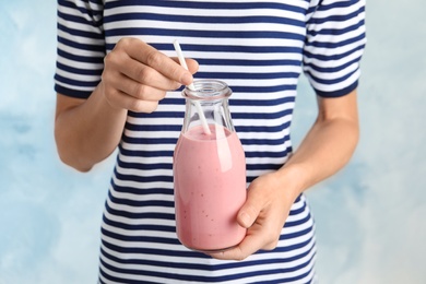 Woman with glass bottle of tasty smoothie on light blue background, closeup