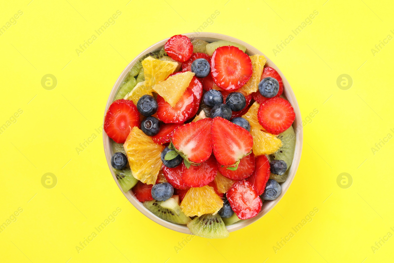 Photo of Yummy fruit salad in bowl on yellow background, top view