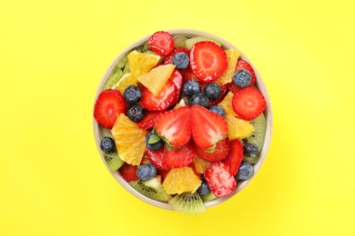 Yummy fruit salad in bowl on yellow background, top view