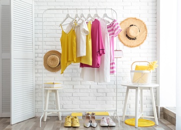 Photo of Wardrobe rack with women's clothes and different shoes at white brick wall in room