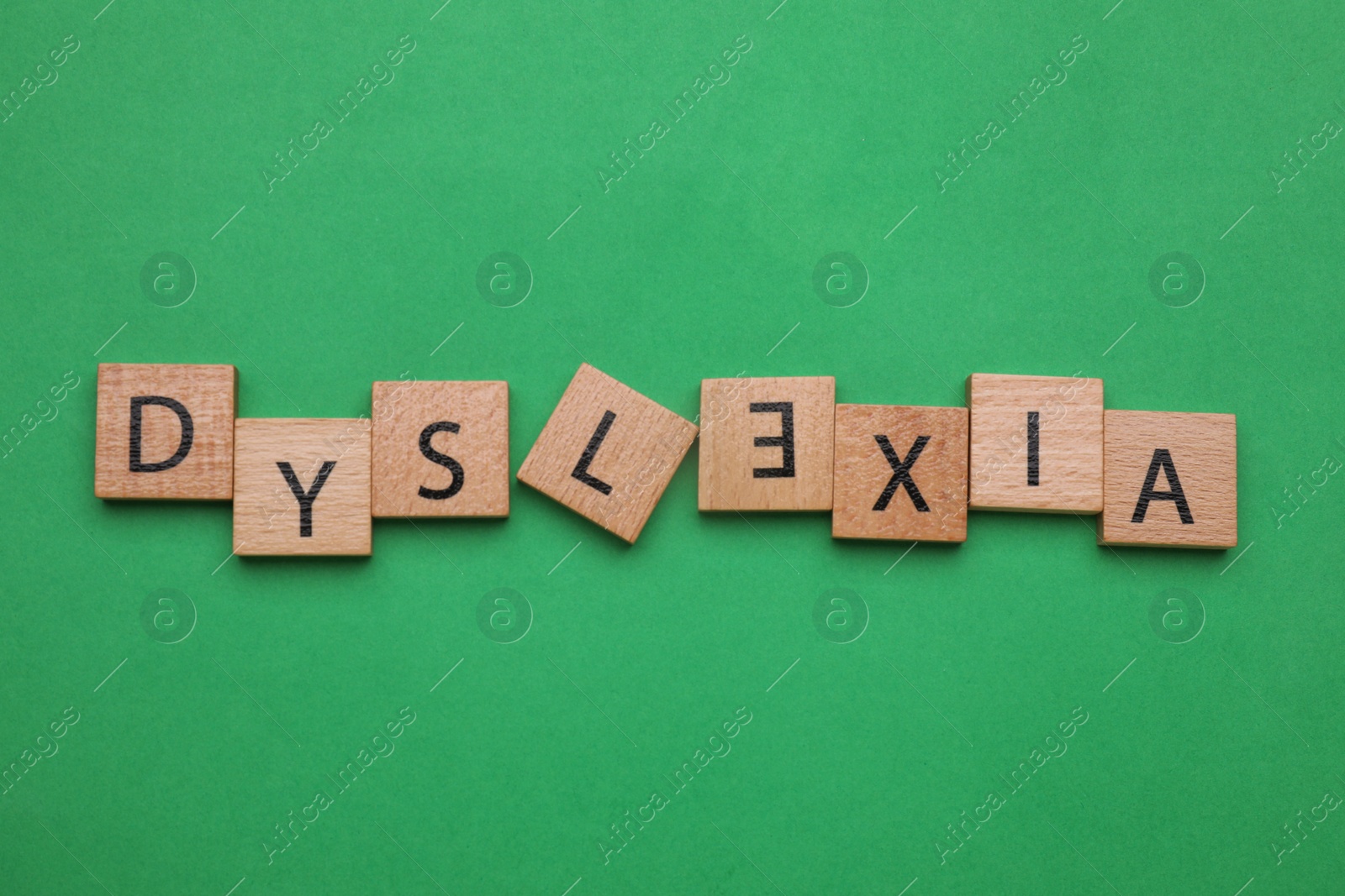 Photo of Word Dyslexia with inverted letter E of wooden tiles on green background, flat lay