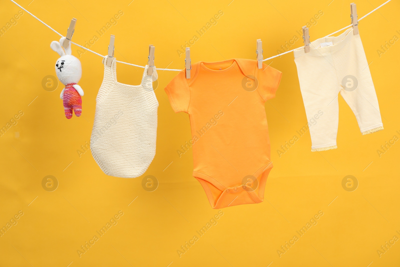 Photo of Different baby clothes and bunny toy drying on laundry line against orange background