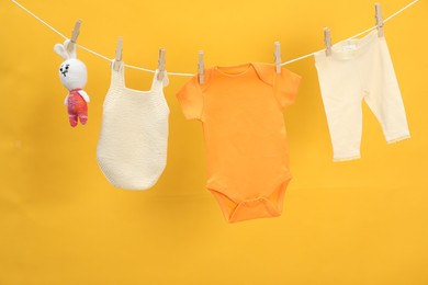 Different baby clothes and bunny toy drying on laundry line against orange background