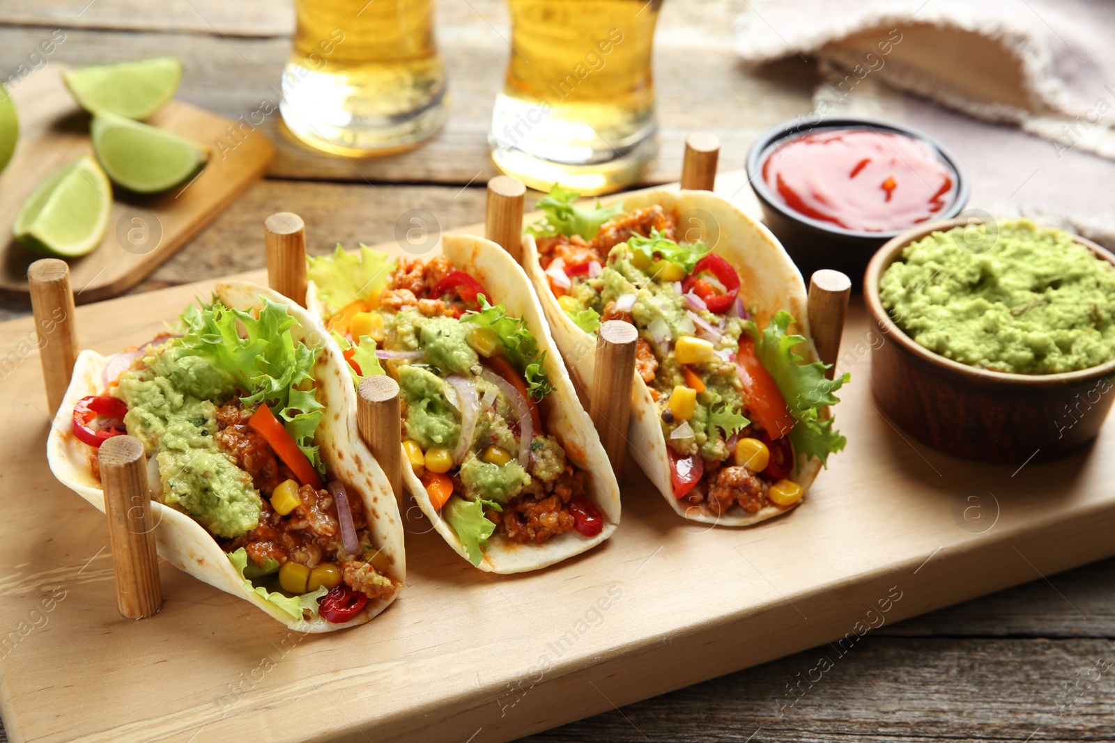 Photo of Delicious tacos with guacamole, meat and vegetables served on wooden table, closeup