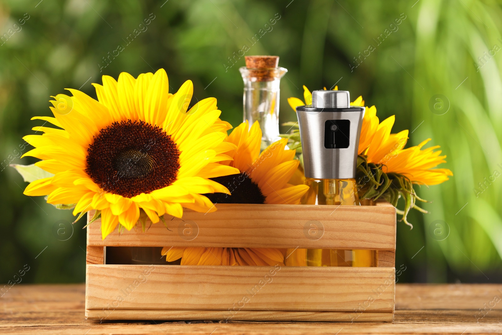 Photo of Crate with bottles of cooking oil and sunflowers on wooden table against blurred background