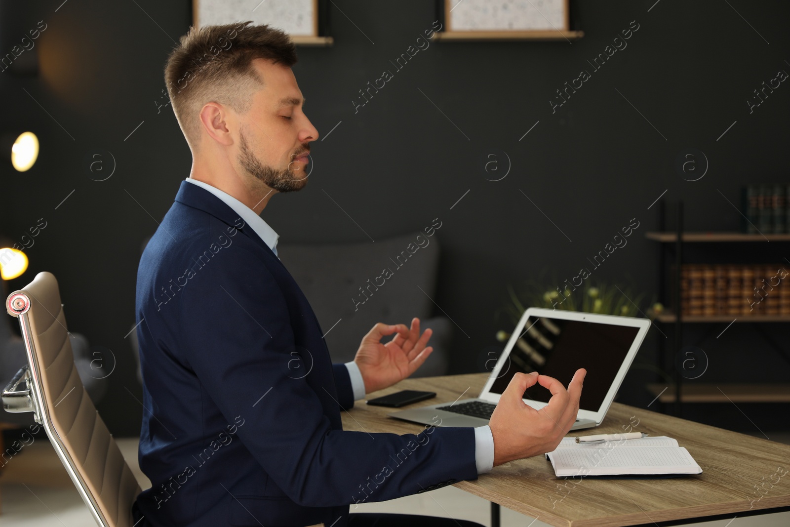 Photo of Businessman practicing zen yoga at table in office