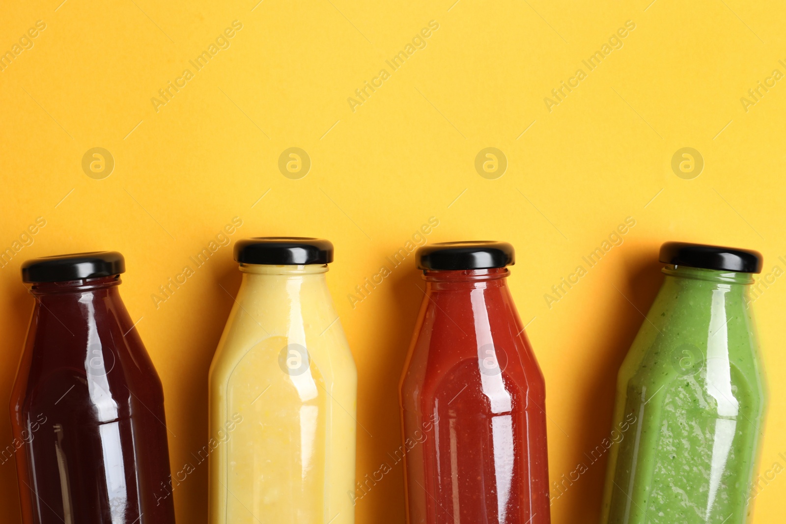 Photo of Bottles with delicious colorful juices on yellow background, flat lay. Space for text