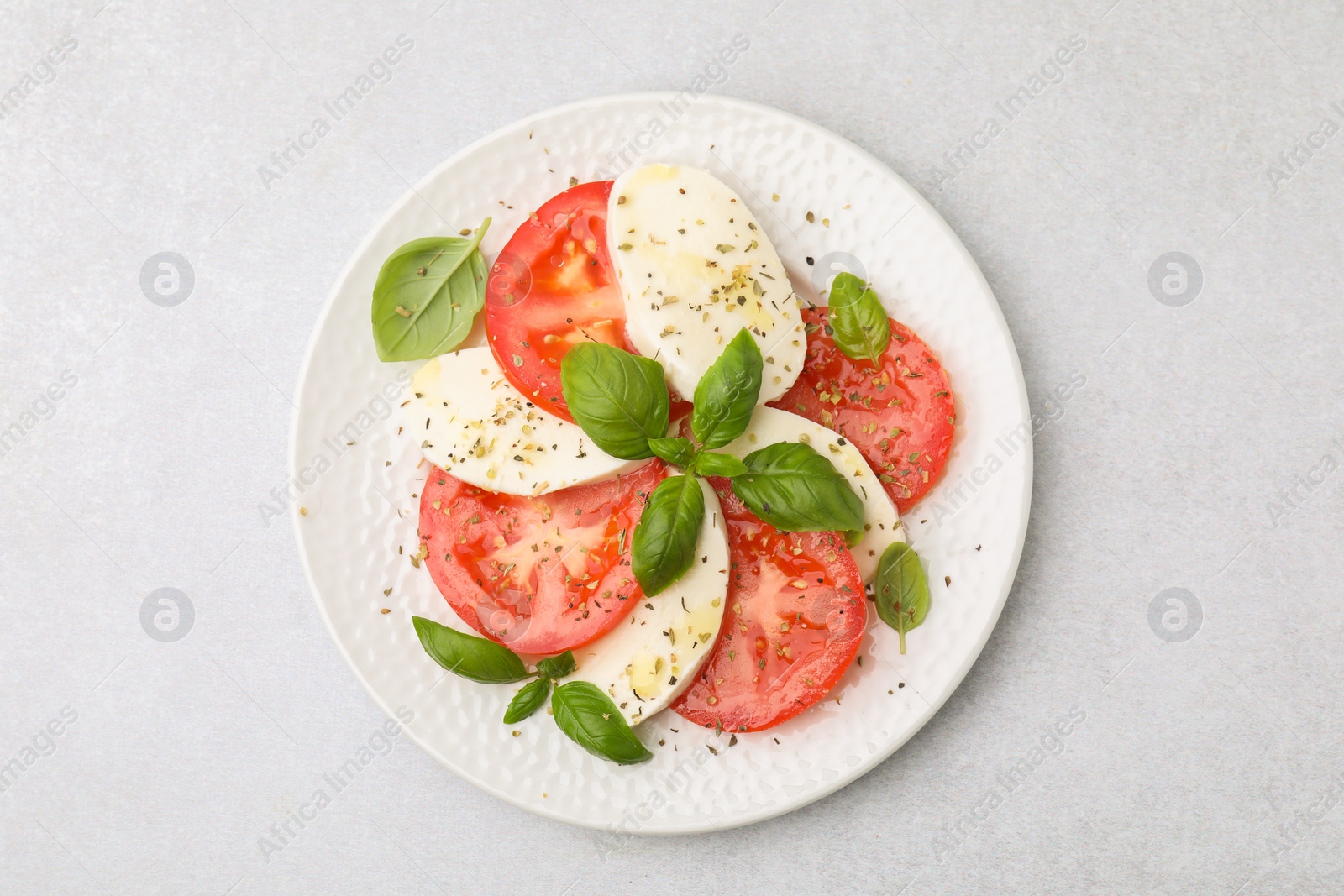 Photo of Plate of delicious Caprese salad with herbs on light grey table, top view