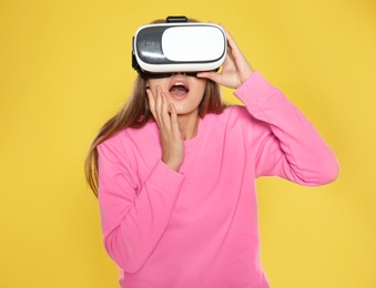 Photo of Emotional young woman playing video games with virtual reality headset on color background