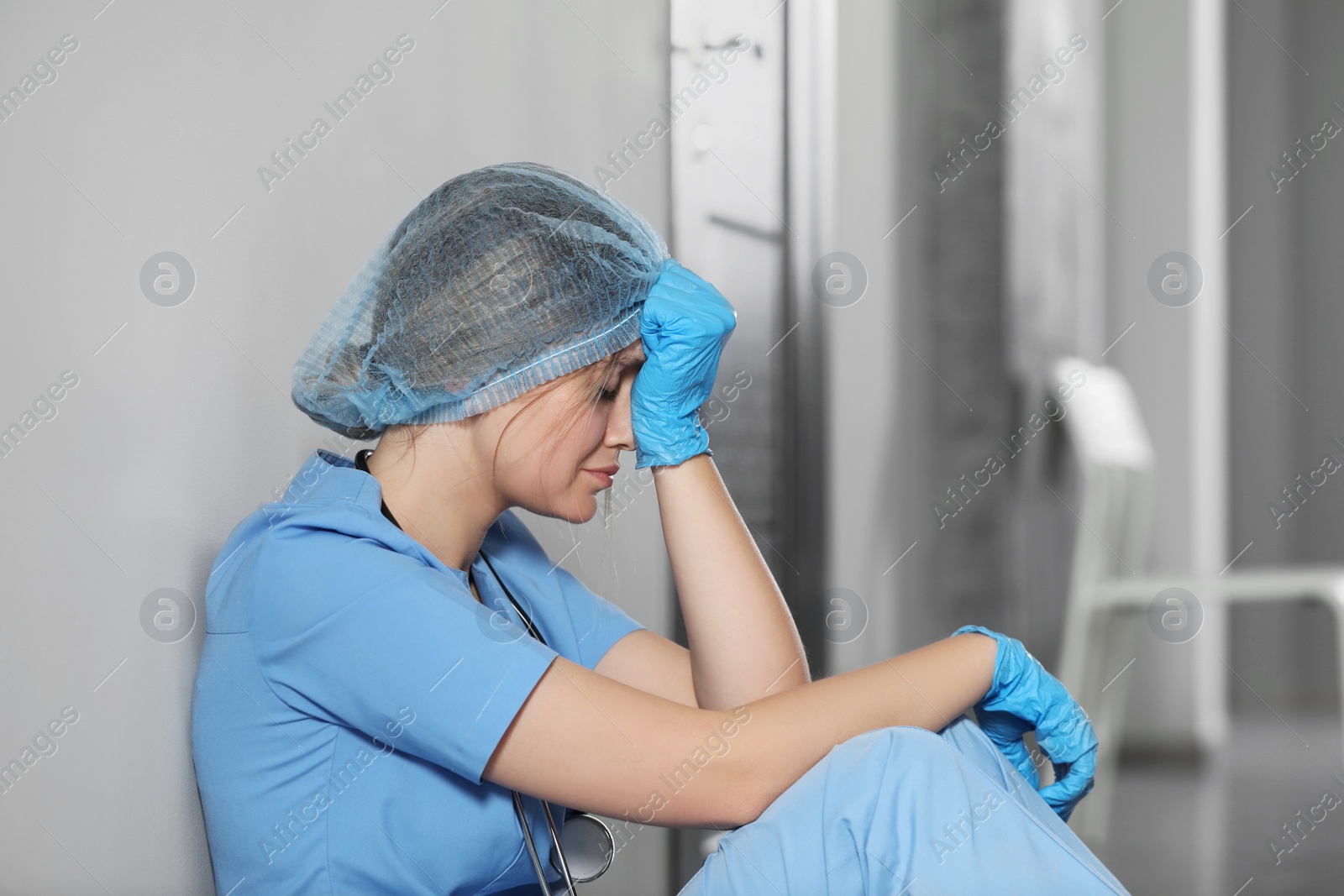 Photo of Exhausted doctor sitting near wall in hospital