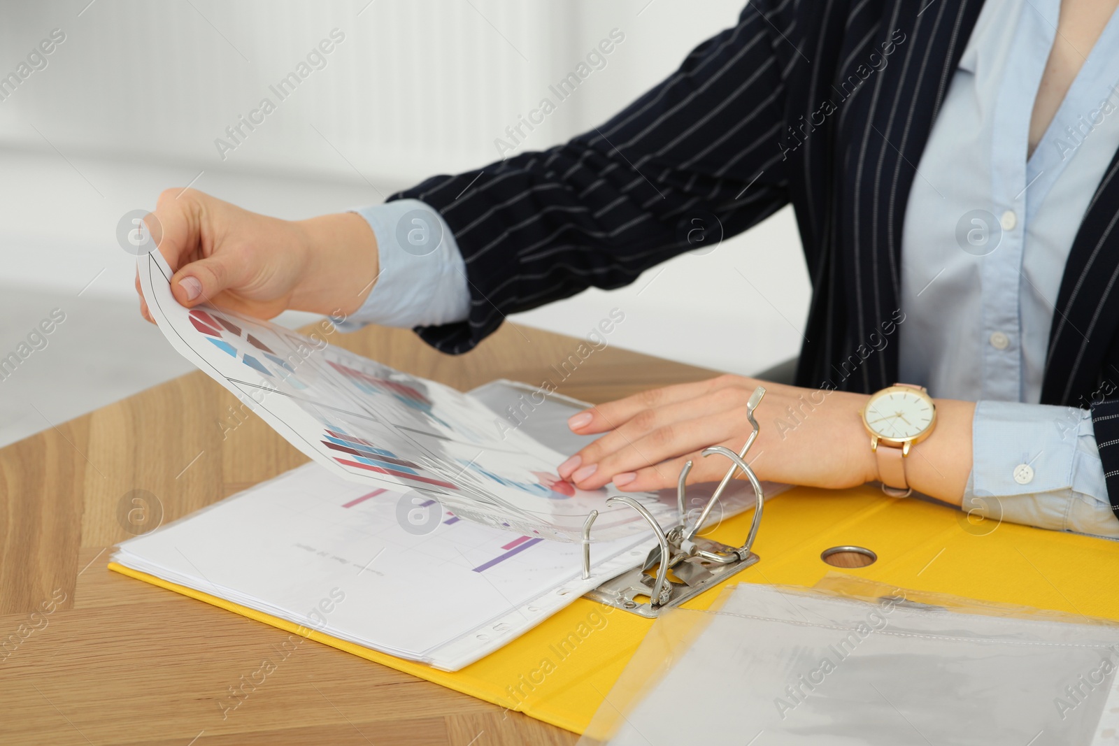 Photo of Businesswoman putting document into file folder at wooden table in office, closeup