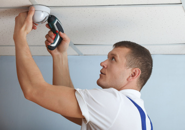 Technician installing CCTV camera on ceiling indoors