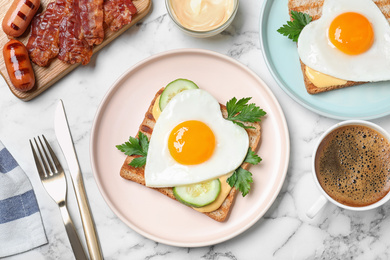 Photo of Tasty sandwiches with heart shaped fried eggs for romantic breakfast on white marble table, flat lay